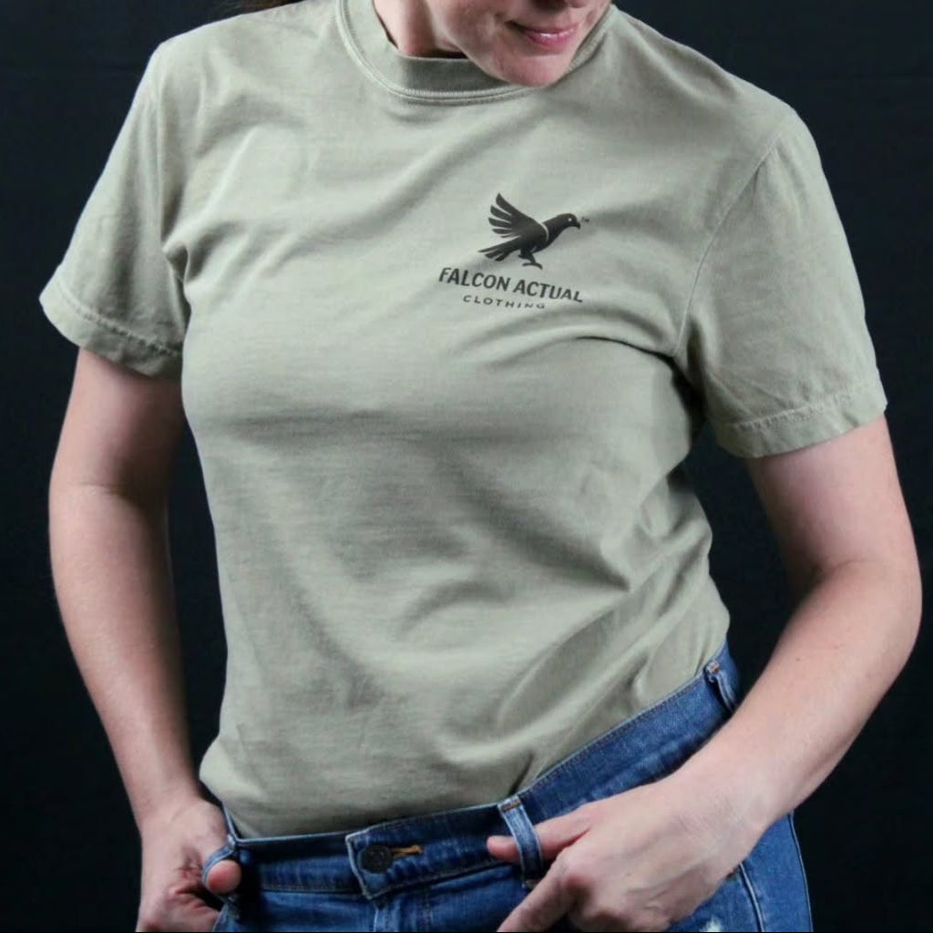 A woman wearing a khaki t-shirt and matching trucker hat with a Falcon Actual logo, posing against a black background.